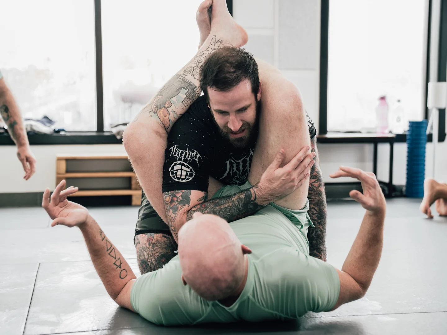 Deux adultes pratiquent le jiu-jitsu no-gi au sol.